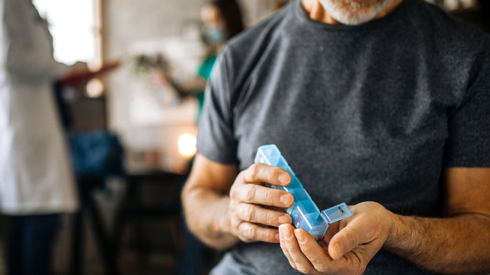 Close-up of a man at home taking medications from a daily pill organizer box.