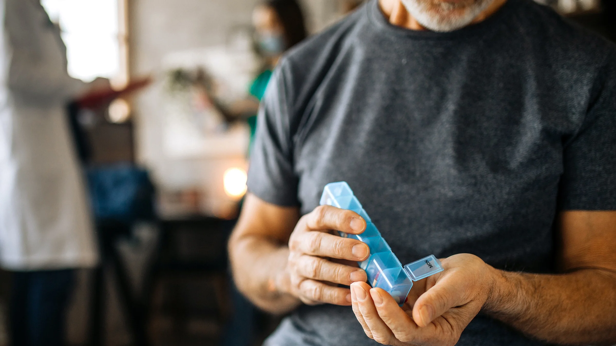 Close-up of a man at home taking medications from a daily pill organizer box.