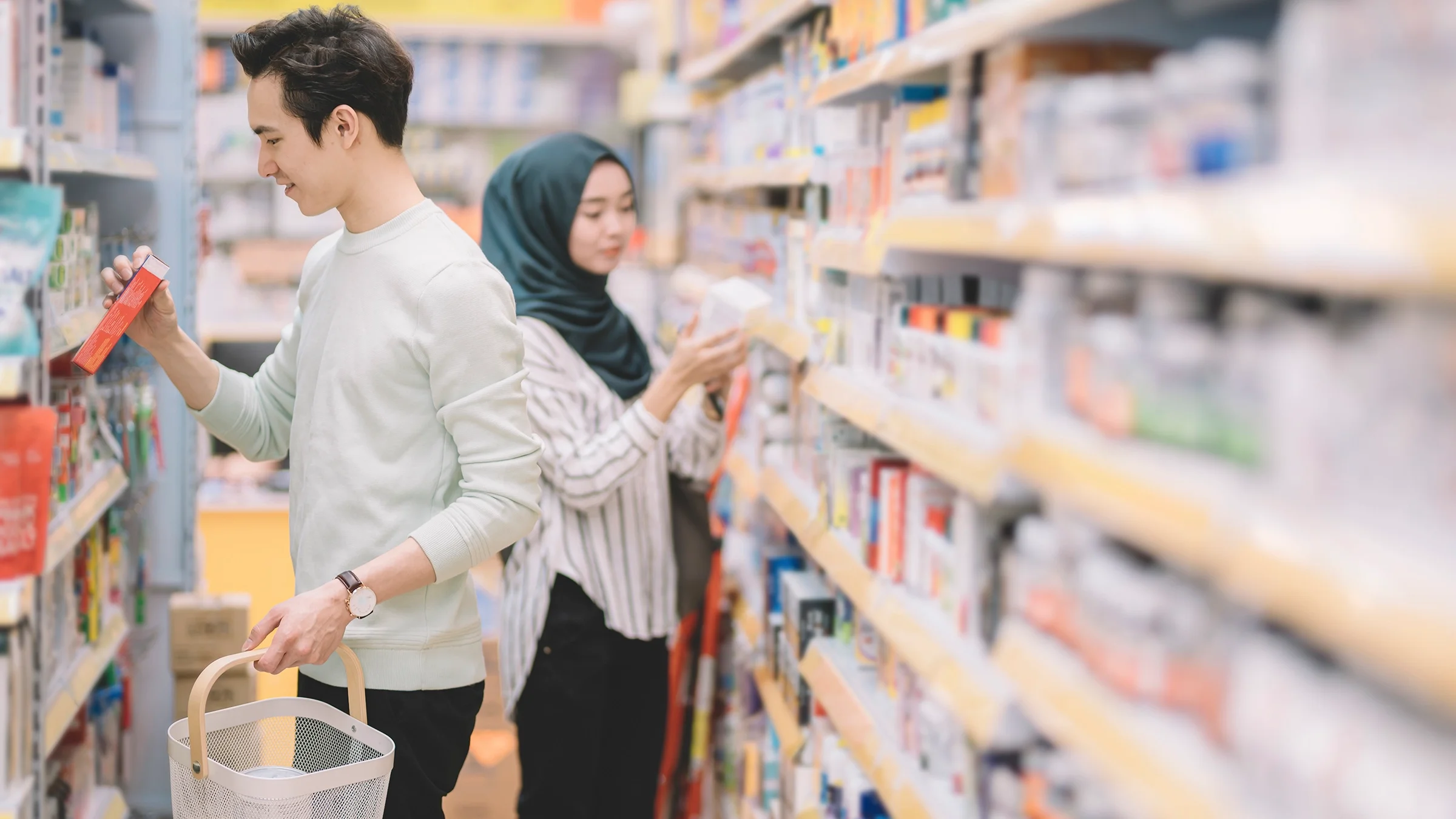 Two people browse medications in the pharmacy aisle.