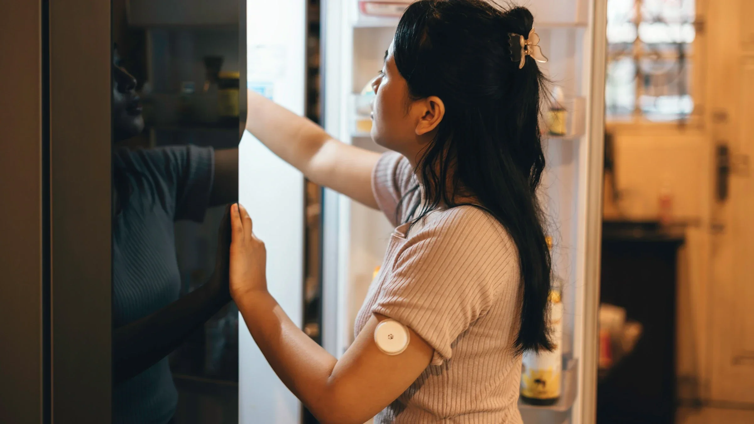 A diabetic adult with an insulin monitor on their arm reaches into their fridge.
rudi_suardi/E+ via Getty Images 