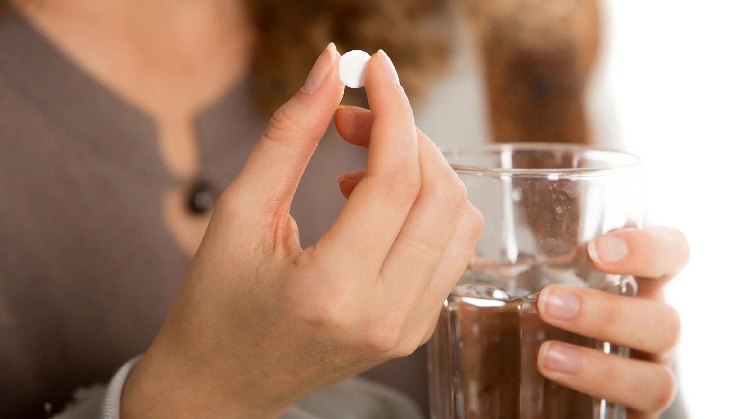 Close-up hand holding one pill and glass of water.