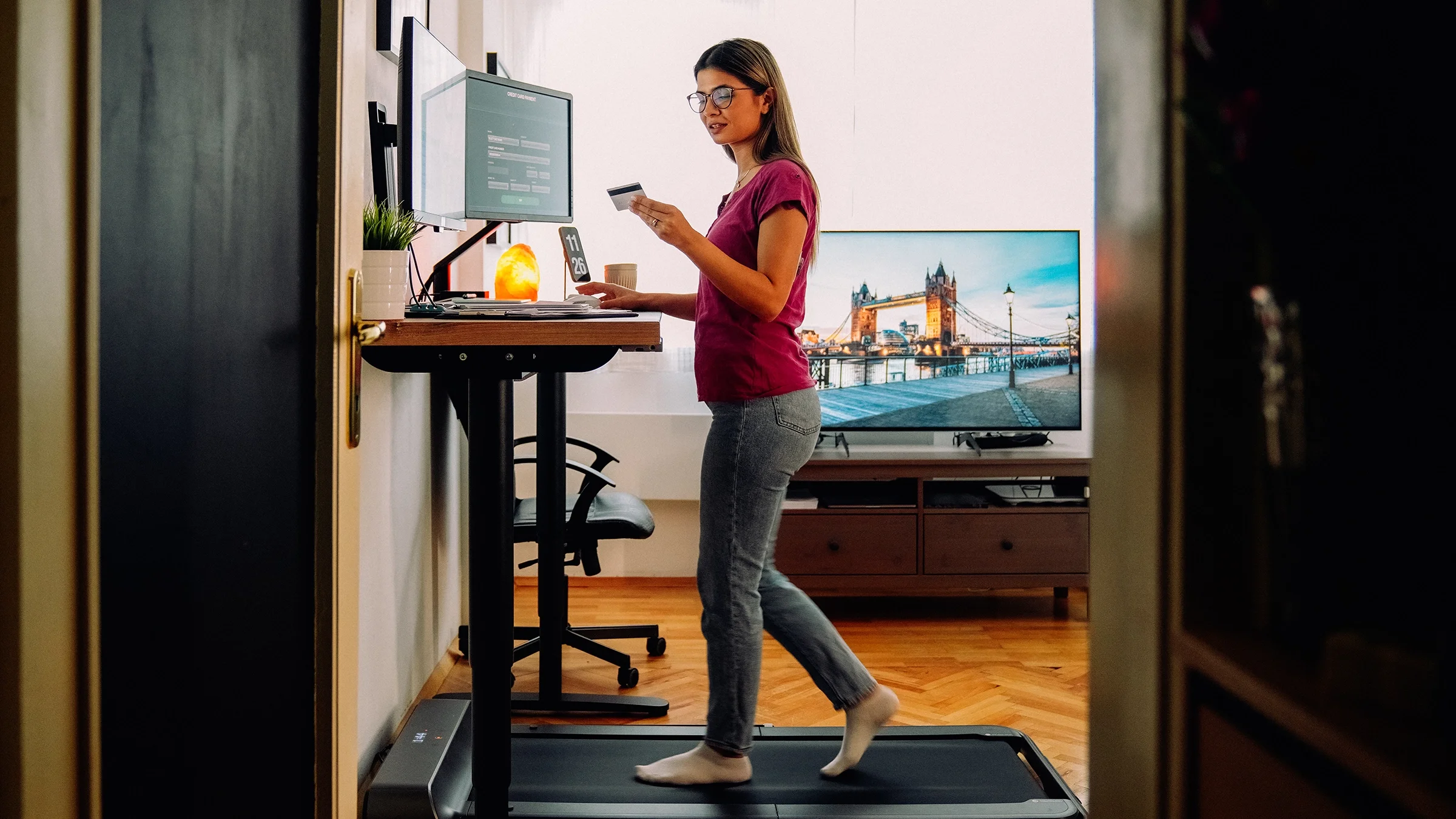 A woman working from home at a standing desk checks her credit card information in order to pay a bill.