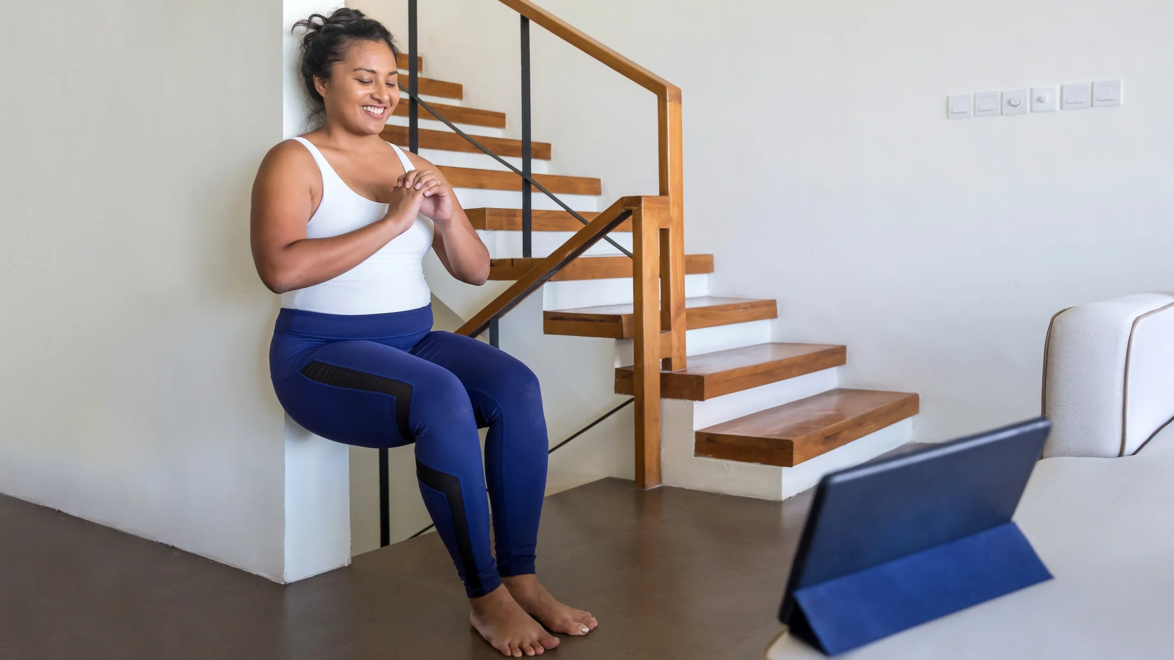 A woman does a wall sit exercise at home.
