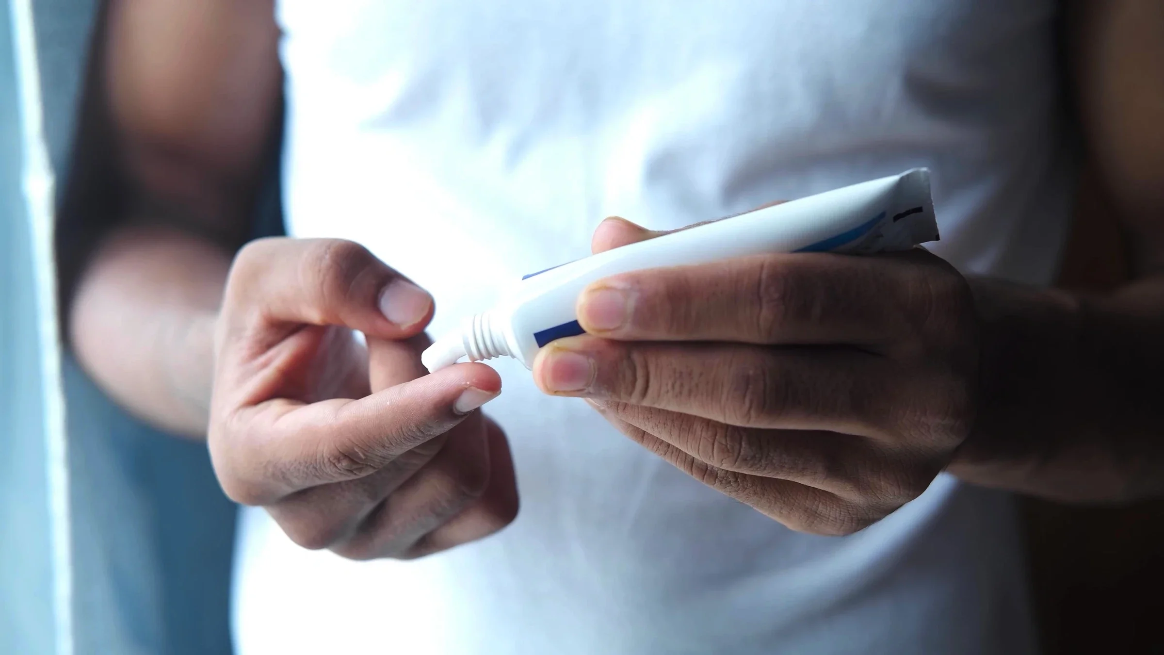 A person squeezes cream onto their finger.