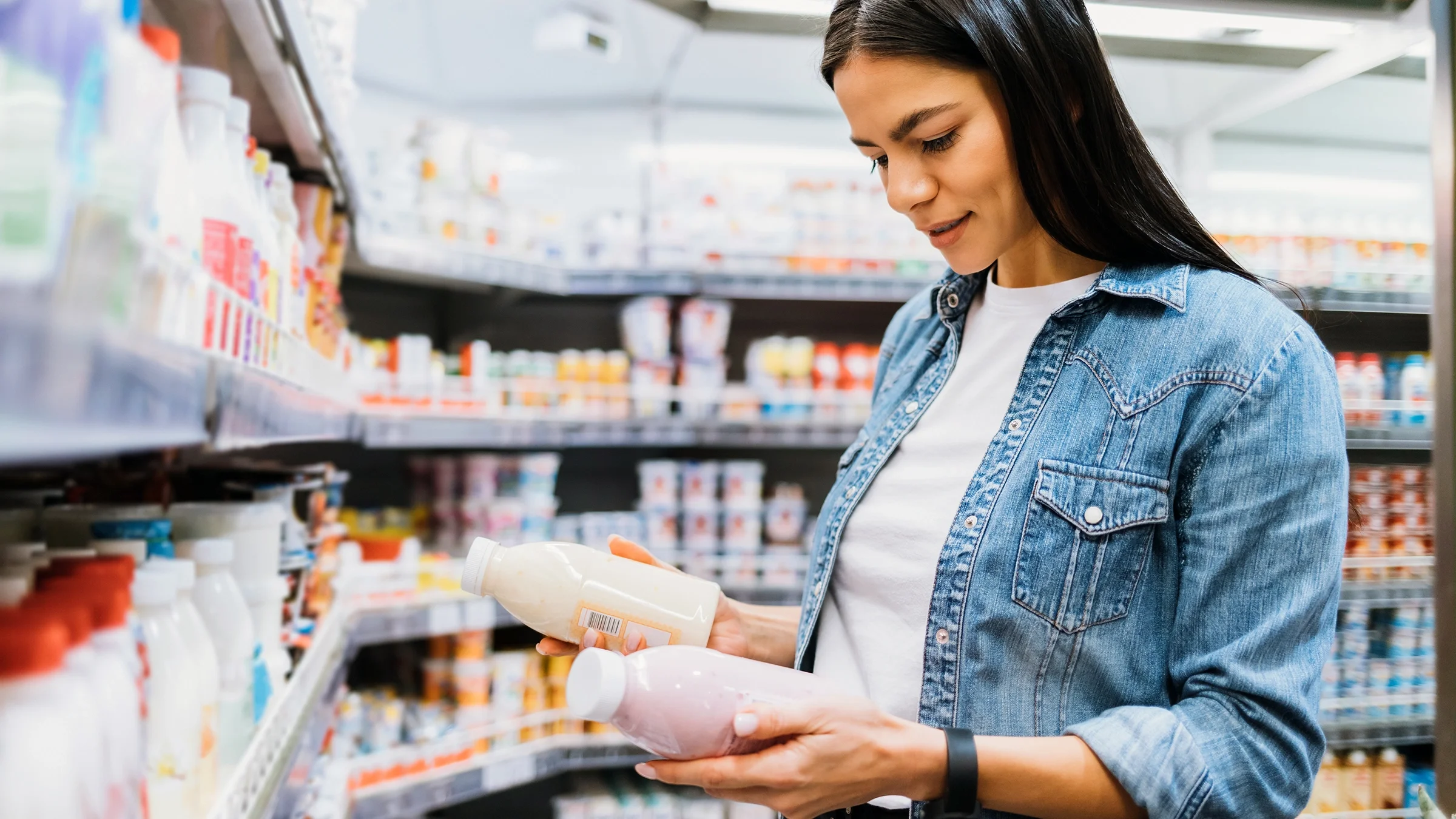 Woman in supermarket holding two bottles of yogurt.