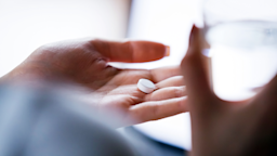 A close-up image shows an adult holding a pill in their hand with water.
fizkes/iStock via Getty Images Plus