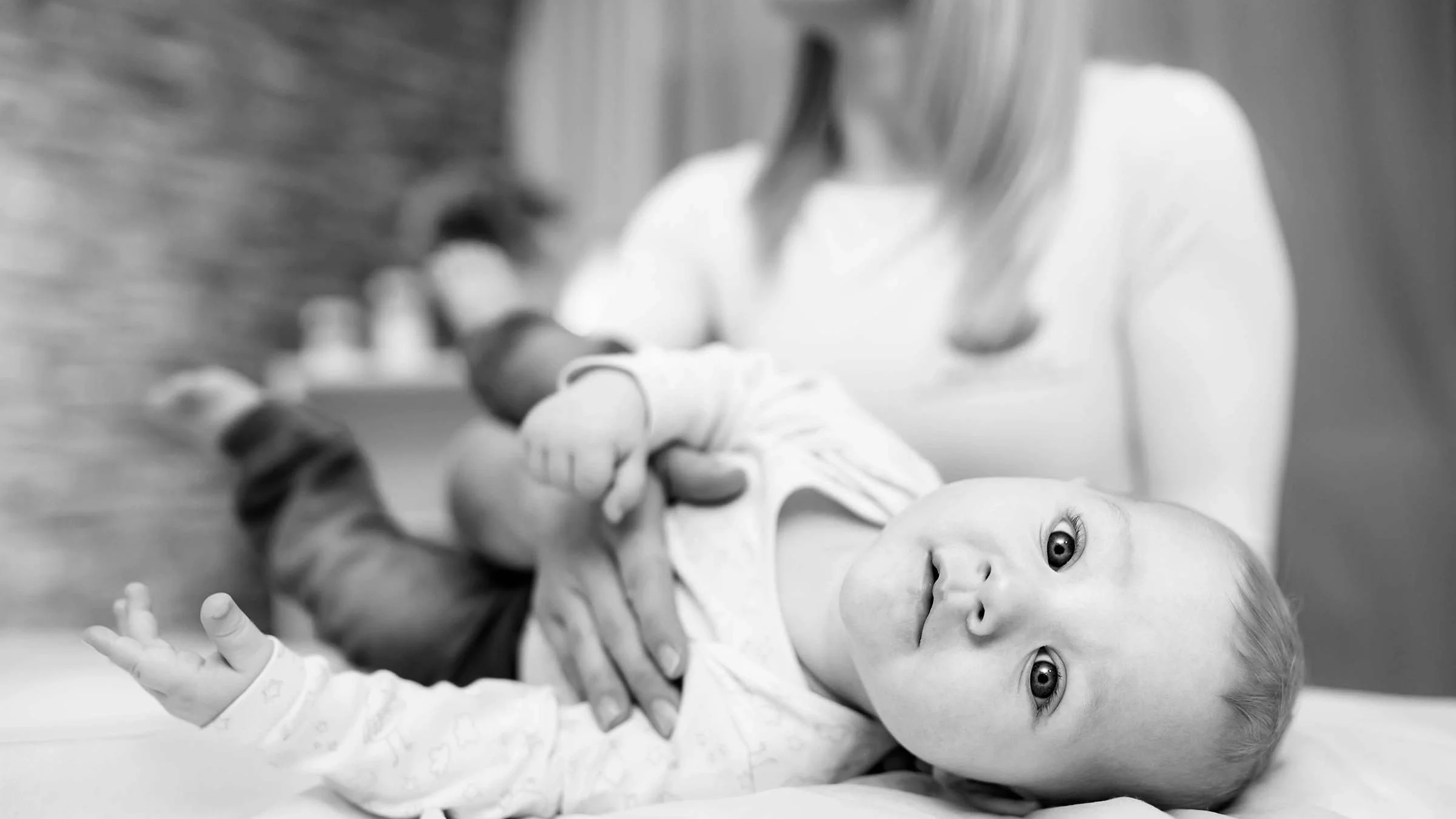 Black-and-white portrait of a baby being treated for chiropractic. The baby is twisting around to look at the camera and craning their neck.