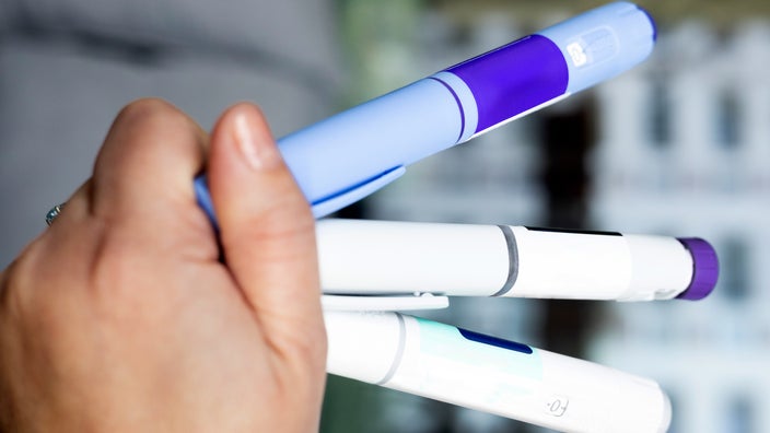 The image provides a close-up view of a hand holding three injection pens.