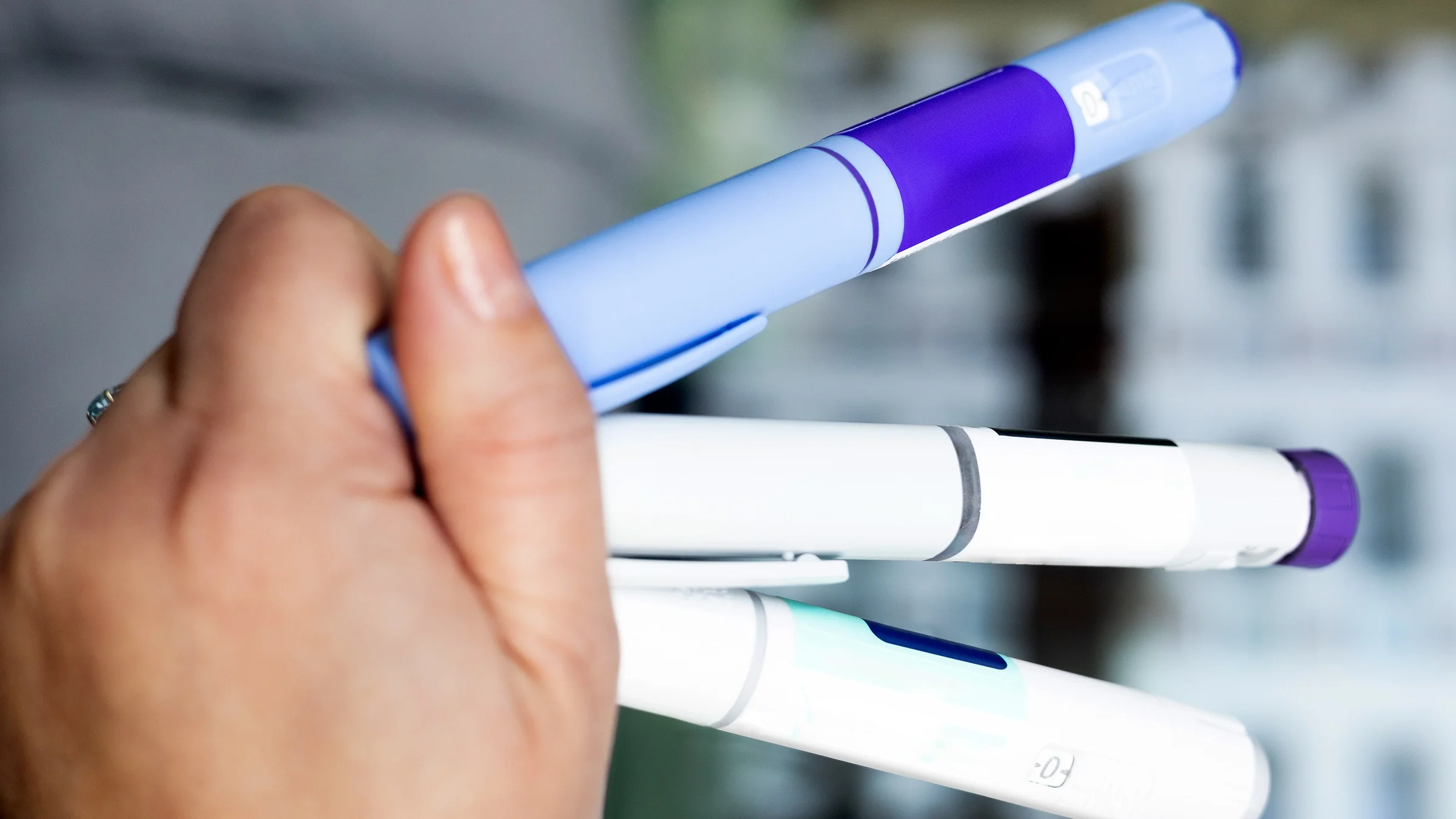 The image provides a close-up view of a hand holding three injection pens.