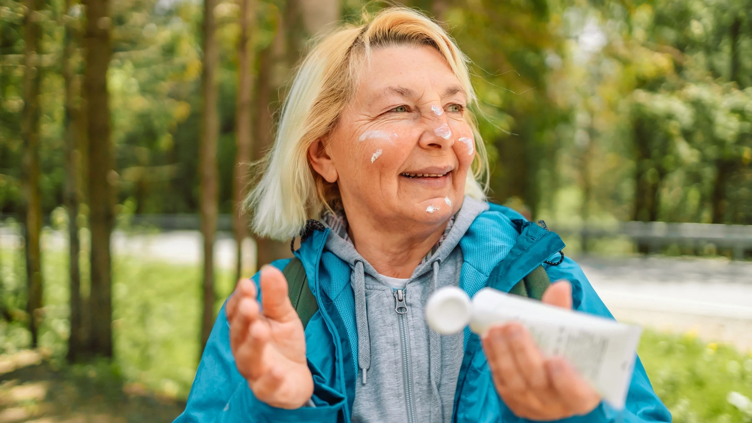 A woman applies sunscreen to her face outdoors.