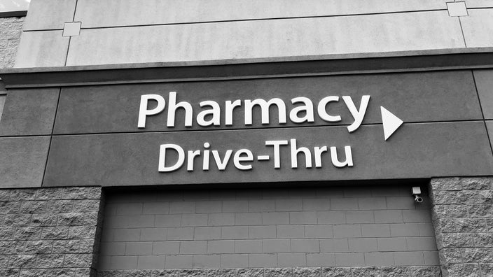 Black and white image of a Drive-Thru Pharmacy sign on the side of a building.