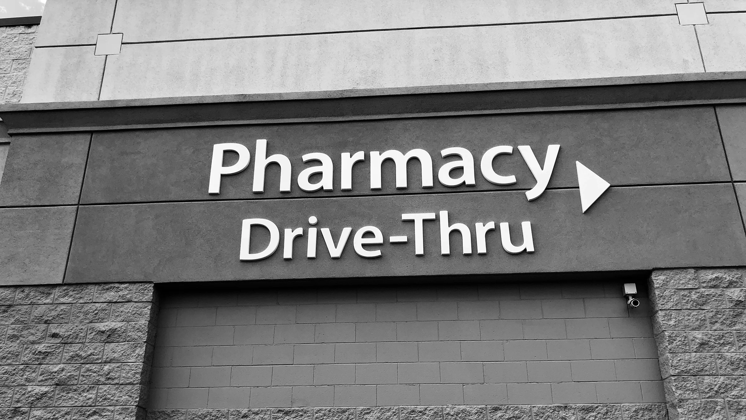 Black and white image of a Drive-Thru Pharmacy sign on the side of a building.