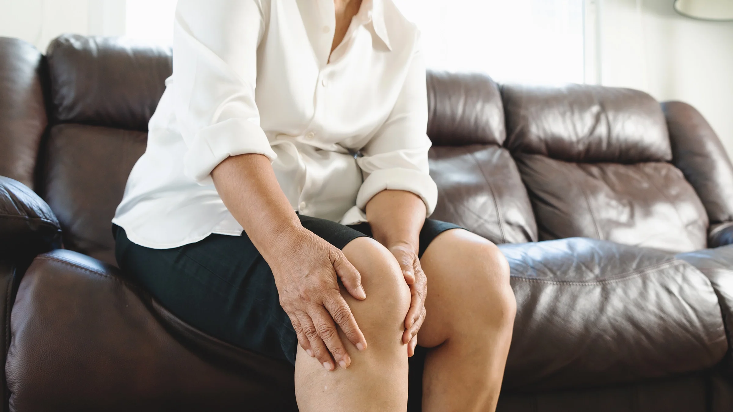 Close-up of woman suffering from knee pain at home.