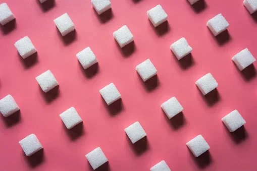 Sugar cubes making a diagonal pattern on a bright pink background.
jastrijebphoto/iStock via Getty Images