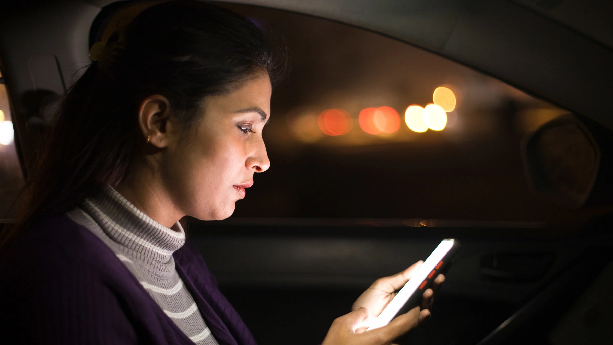 A woman uses a mobile phone in her car at night.