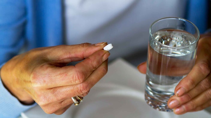 A close-up of a woman taking a pill and holding a glass of water.
