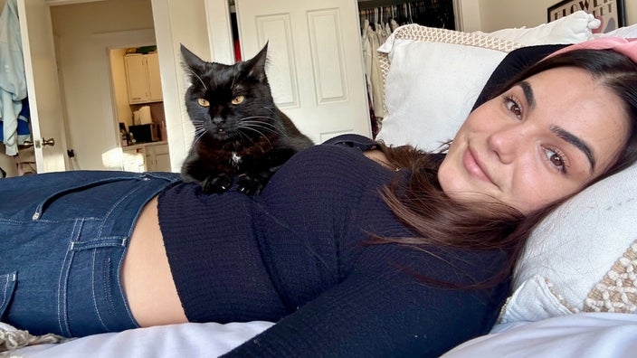 Sarah Chiappetta is pictured lying on her bed in her apartment, with her cat Harper on her stomach.