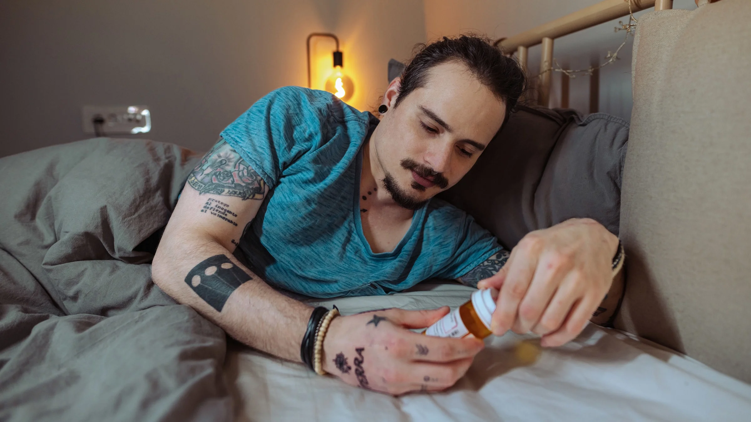 A man reading a pill bottle in bed.