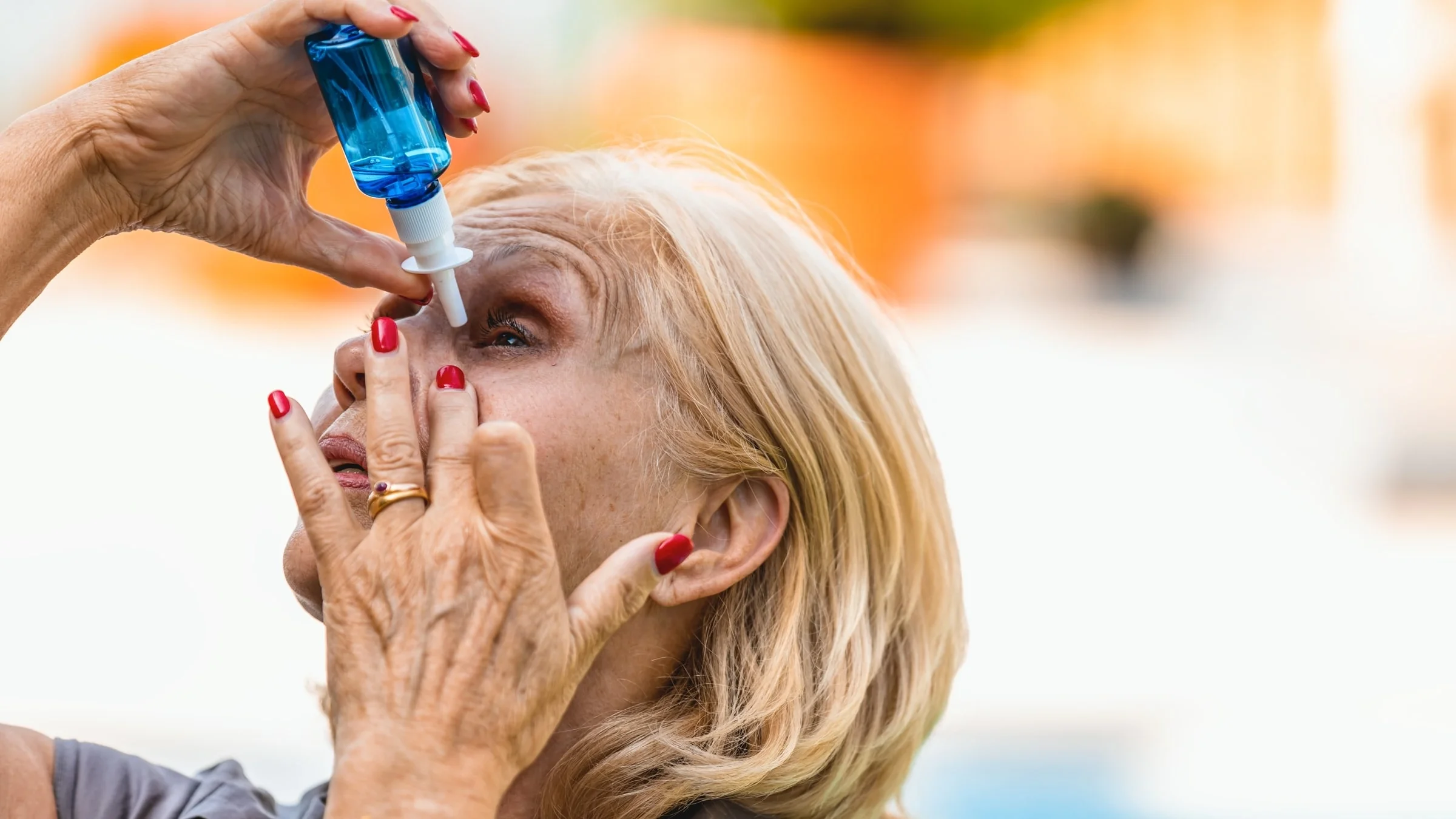An older adult using eye drops.