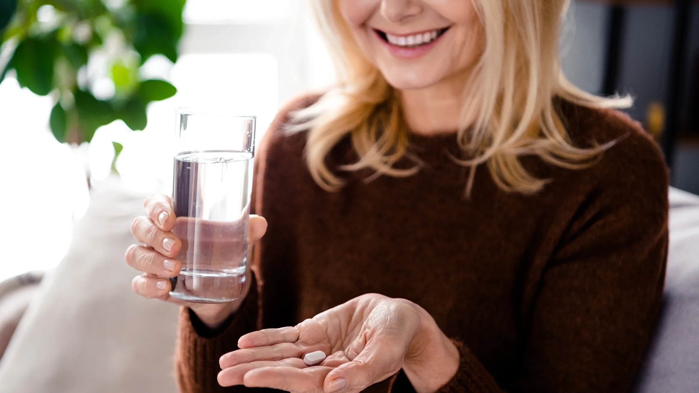 A woman gets ready to take her medication as she holds a glass of water.