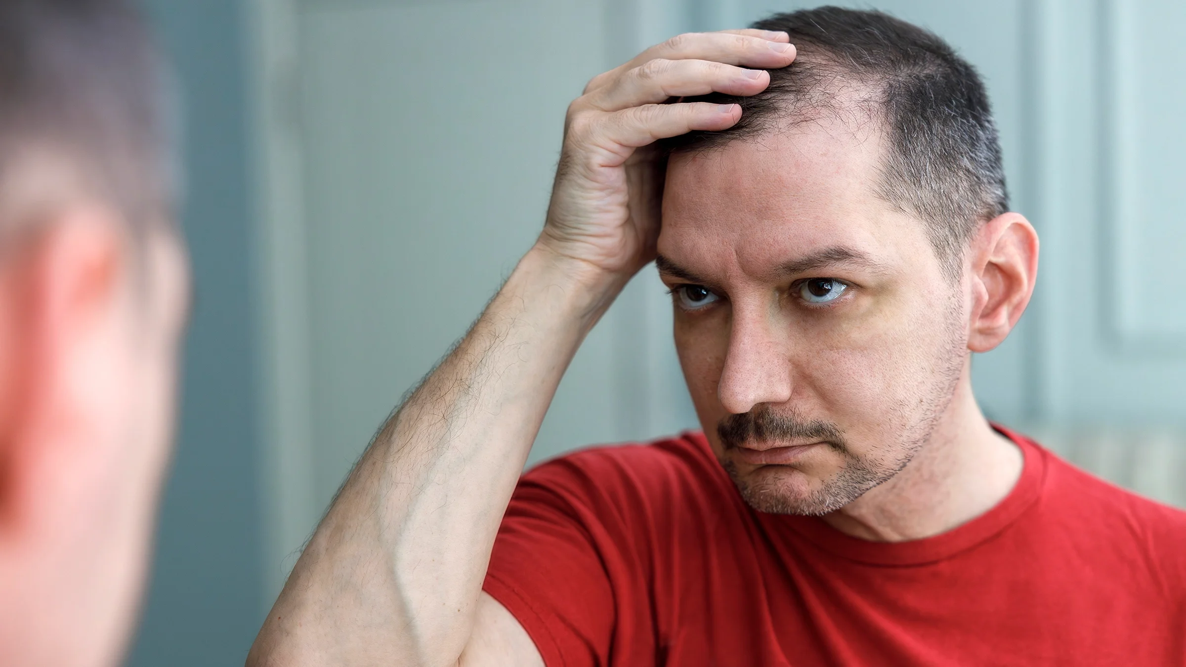 A man checks his hair line in the mirror.