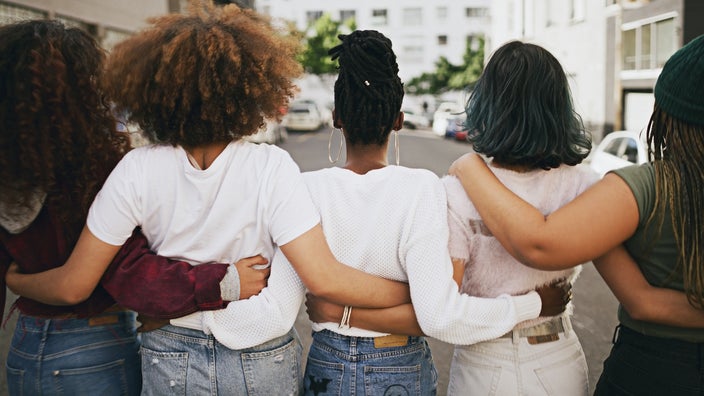 Young friends lined up with their arms around each other. We are looking at their backs.
