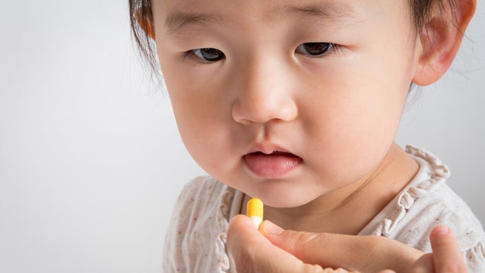Parent giving their baby an antibiotic pill that is yellow and white.