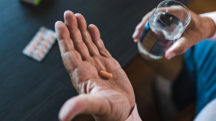 A man prepares to take a pill with a glass of water.