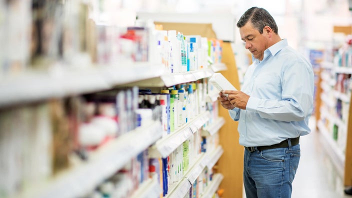 Man reading back of medicine packaging at a pharmacy.