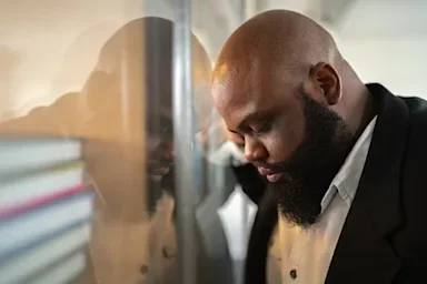 Young Black man resting his head on the office window with a sad depressed look on his face.
FG Trade/E+ via Getty Images
