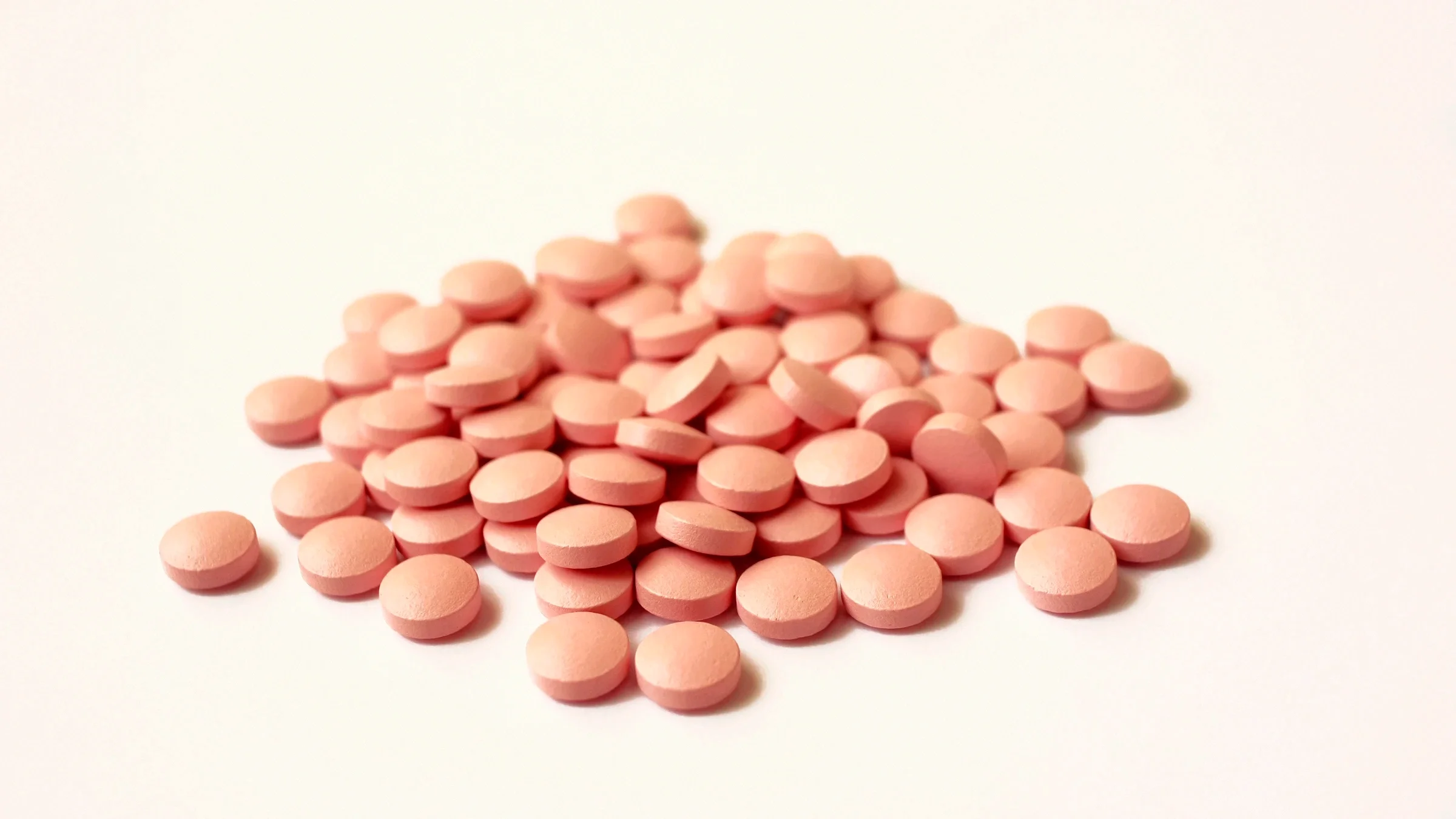 Pile of round, pink pills on a light-colored background.