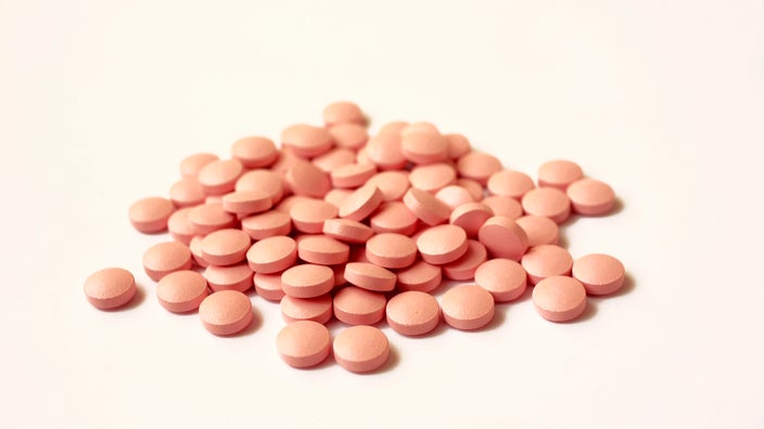 Pile of round, pink pills on a light-colored background.