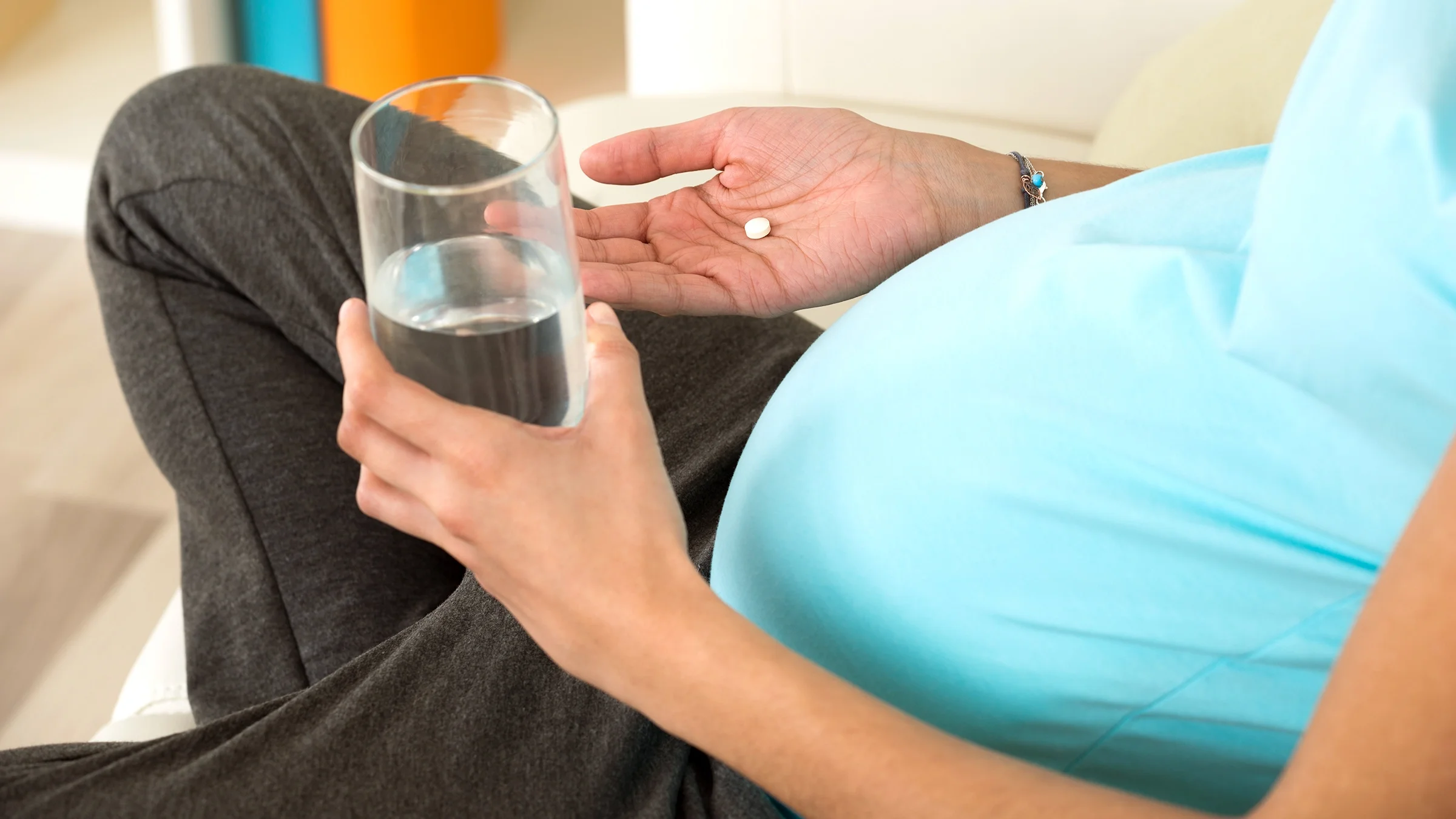 Cropped shot of a pregnant woman taking a small round white pill. She has a glass of water in one hand.