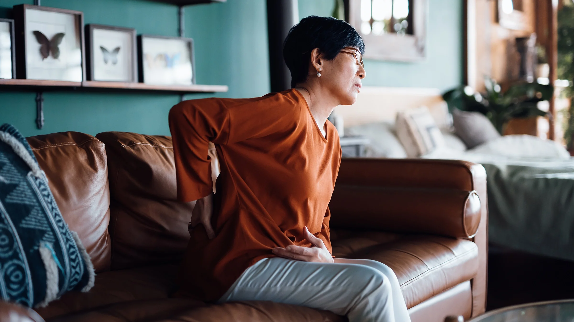 Senior woman experiencing back pain as she sits on the couch at home.