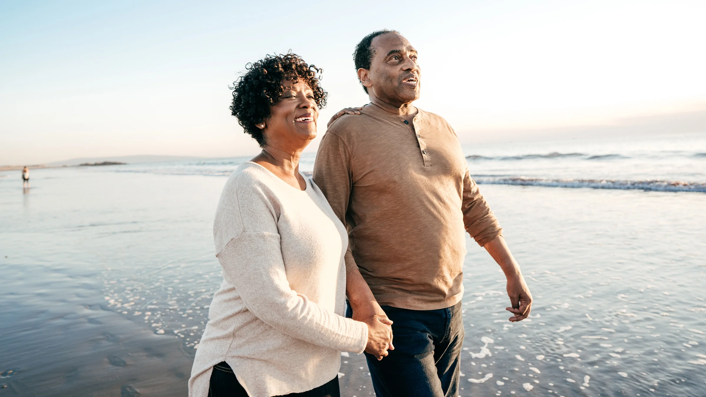 Senior couple walking on the beach holding hands and smiling.