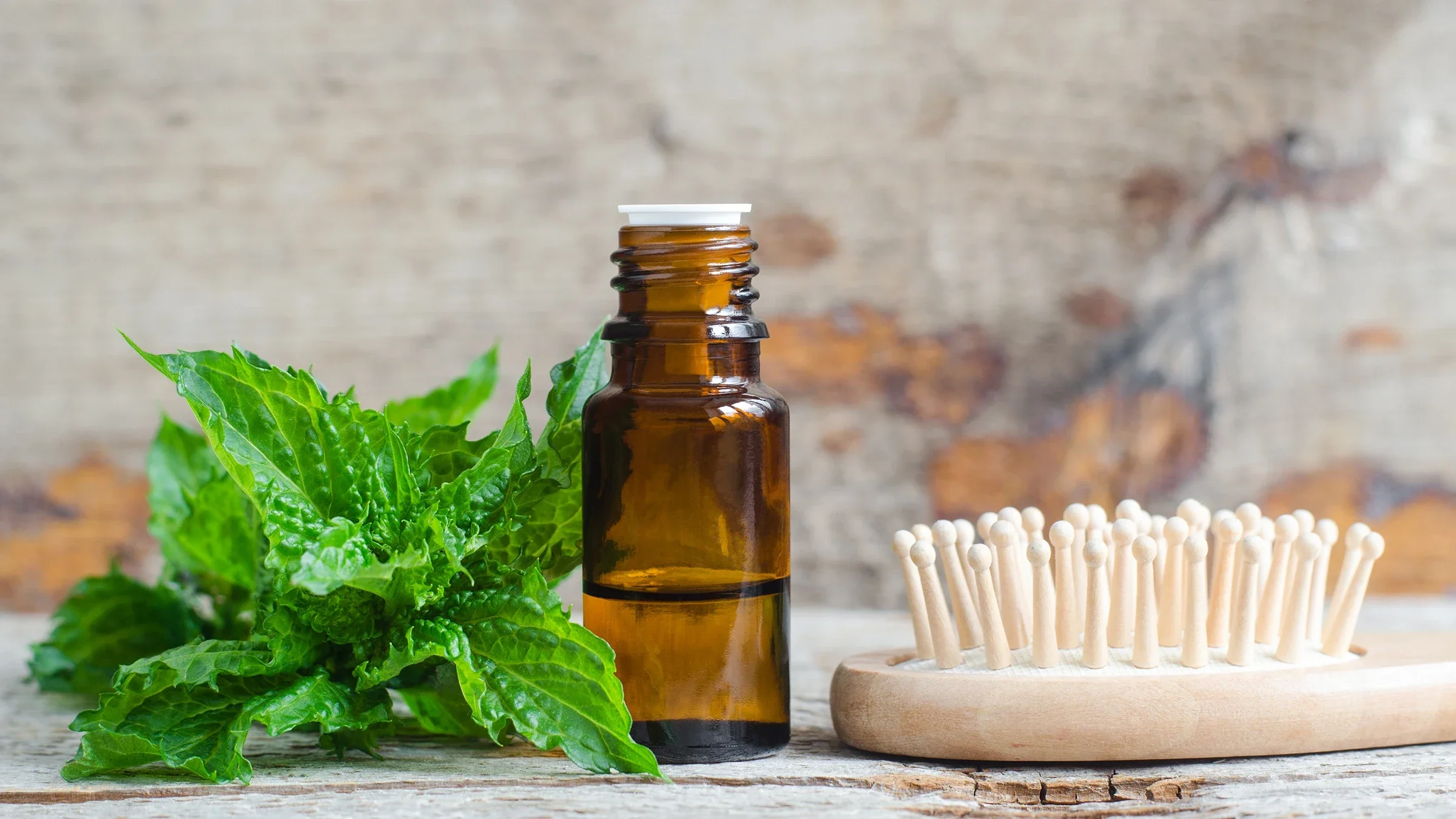 A small bottle sits next to a sprig of mint and a wooden hair brush
kazmulka/iStock via Getty Images Plus 