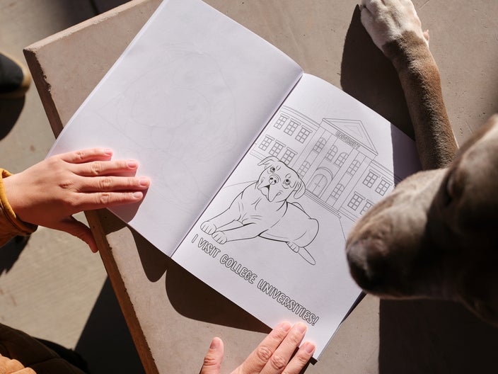 Duke the therapy dog is pictured next to an open coloring book where he’s featured in an illustration that says: “I visit college universities!”