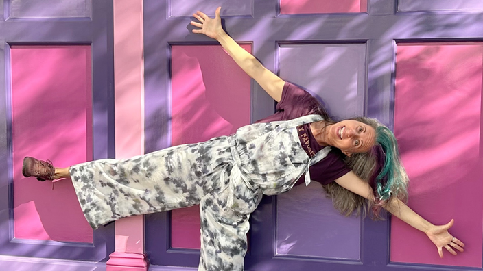 Jean Franzblau is pictured leaning with both arms and one leg outstretched in front of a colorful wall in a snapshot.