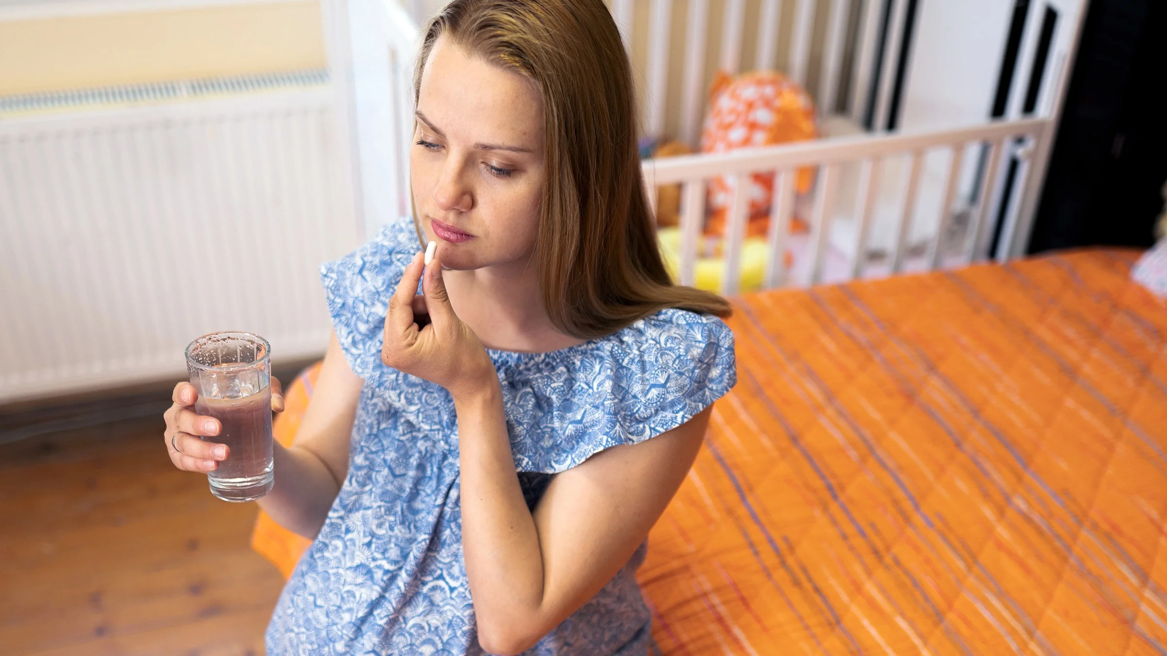 A pregnant person is taking a pill on her bed.