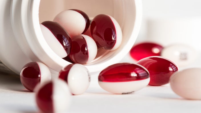 Red and white gel capsule pills spilling out of a white medicine bottle.