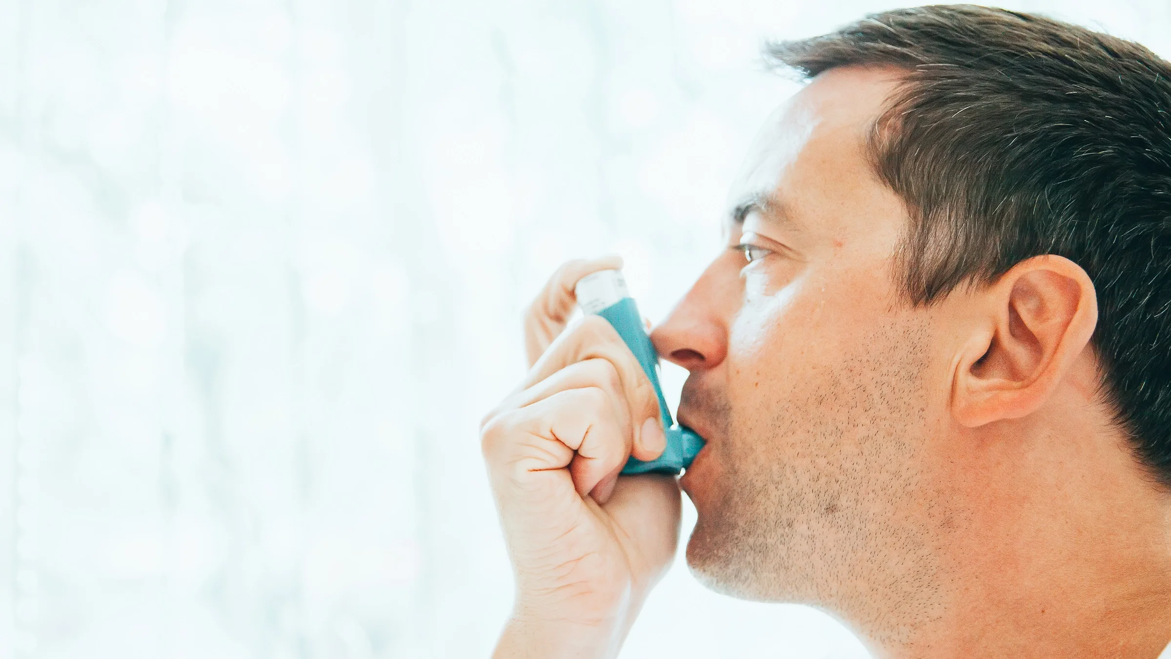 Close-up of a man using an inhaler, side profile.
