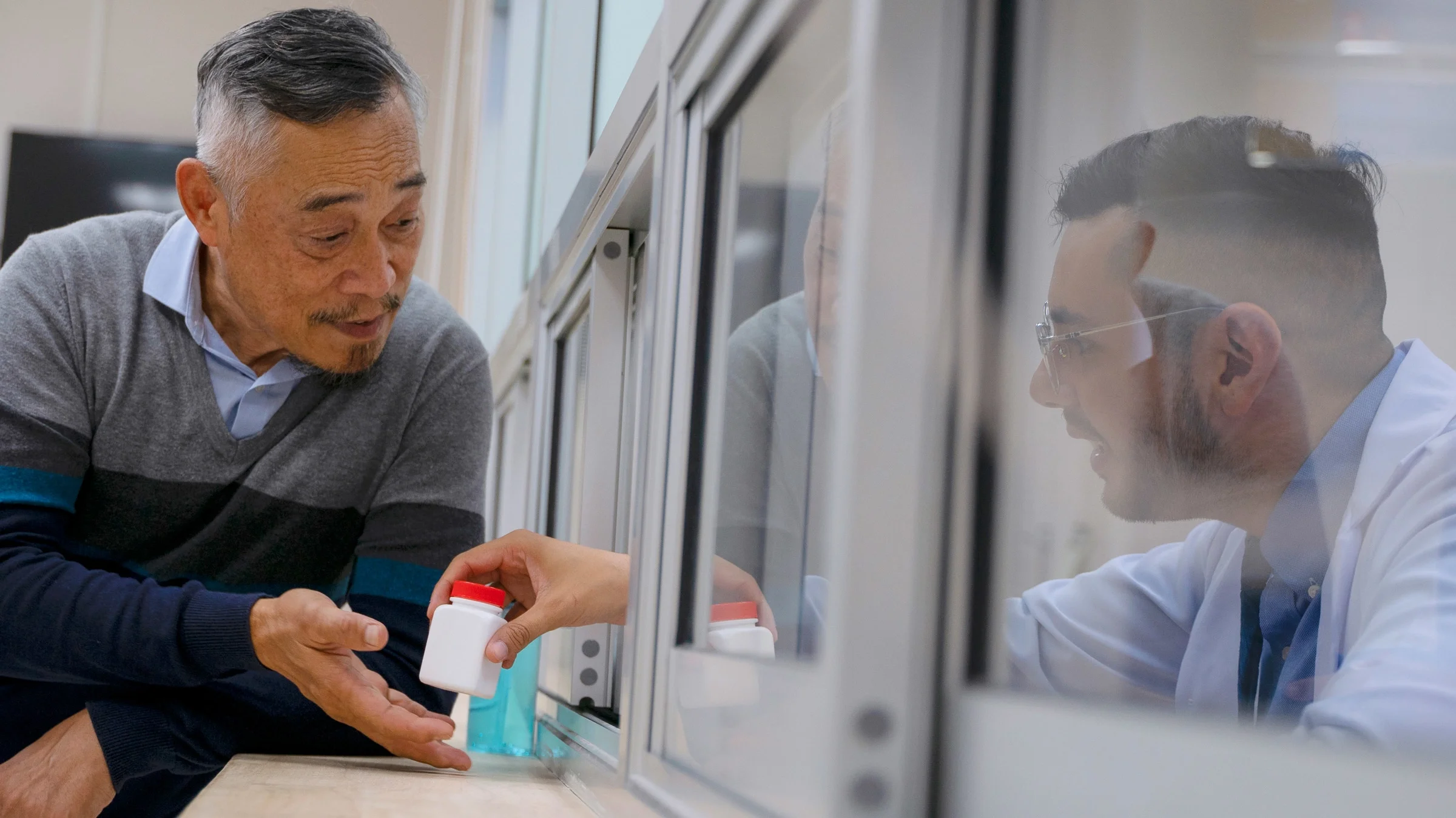 A person picking up a prescription at a pharmacy window.