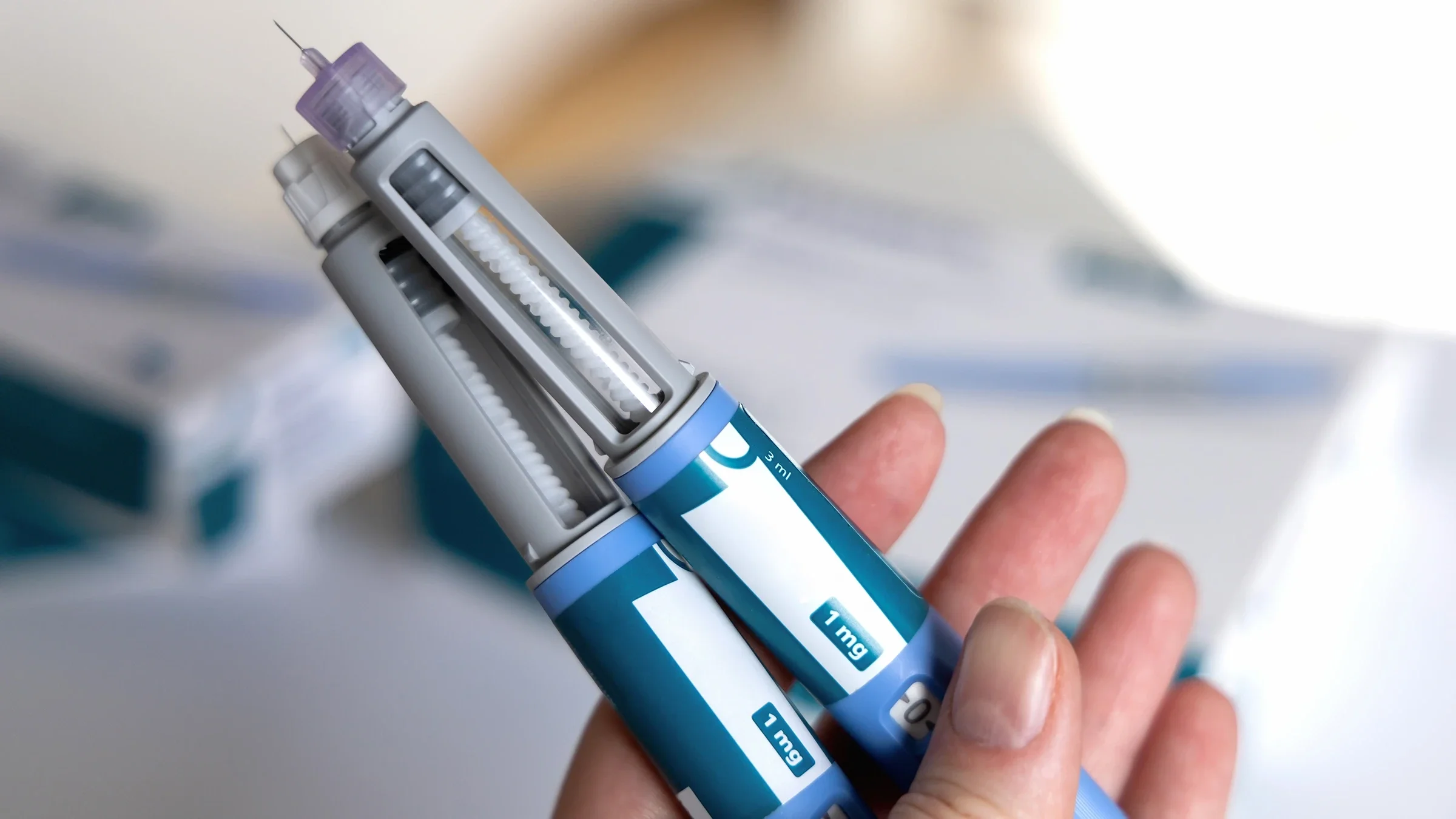 A hand, in close-up, holds two semaglutide pens.