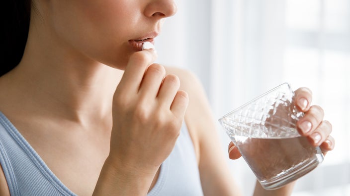 Cropped shot of a woman taking a large white round pill with a glass of water.