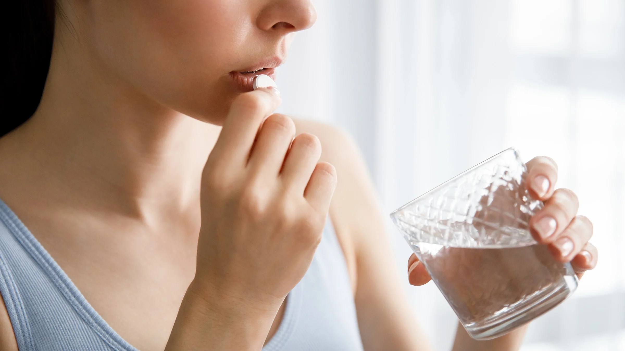 Cropped shot of a woman taking a large white round pill with a glass of water.