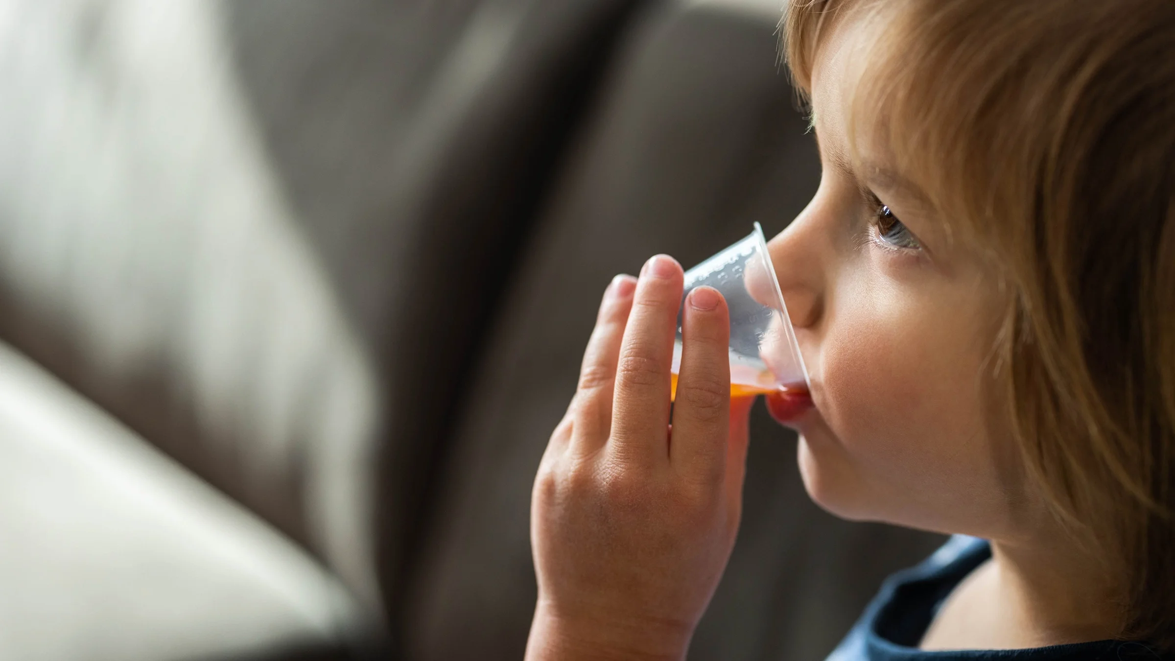 Child taking medicine from a liquid medicine cup.