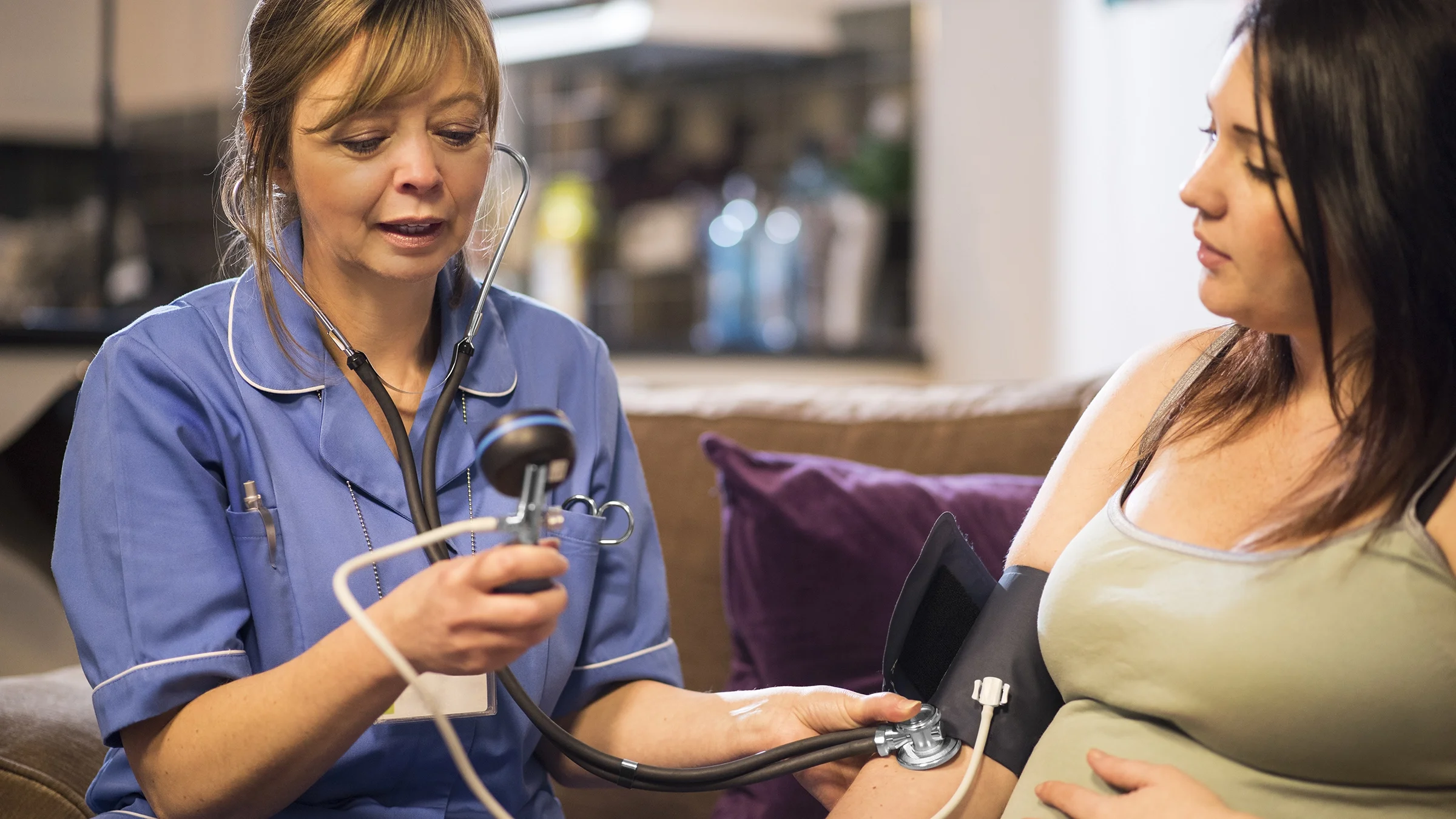 A midwife takes a pregnant woman’s blood pressure during a home visit.