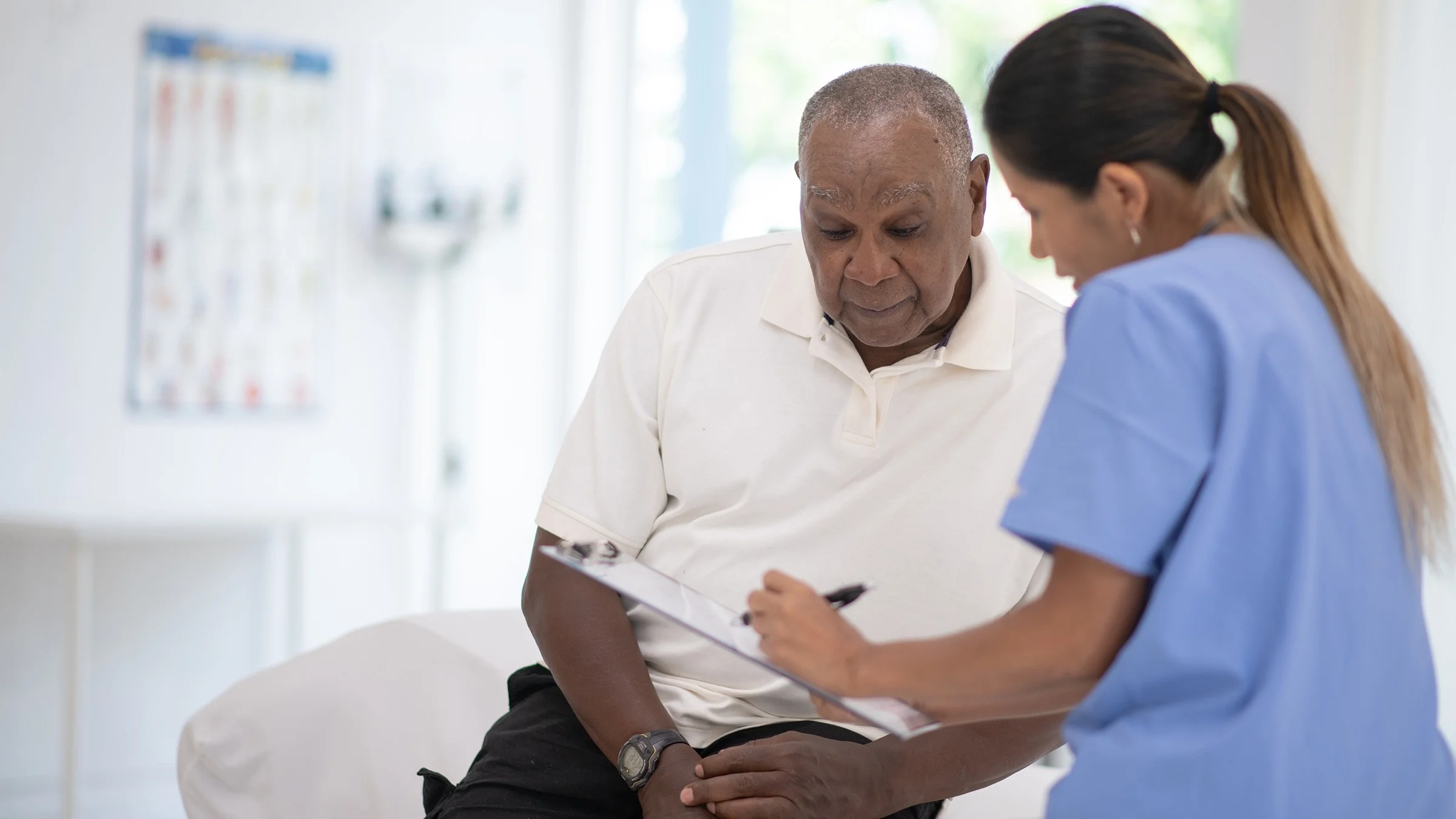 Elderly man reviewing his medical chart with the nurse in an exam room.