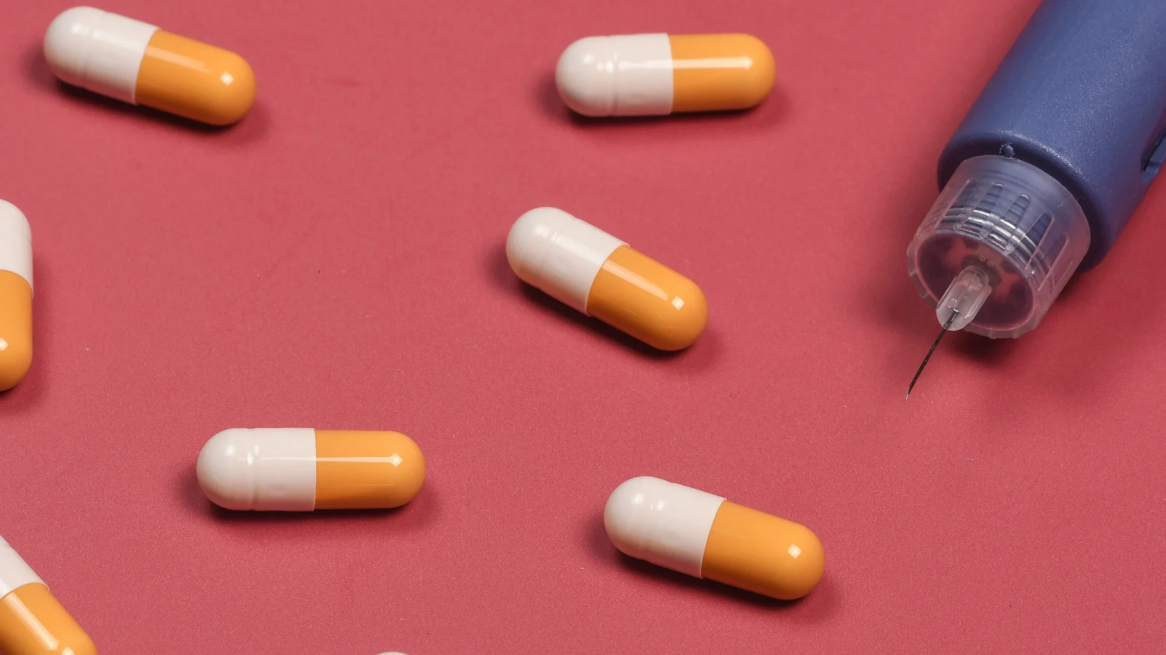 An insulin pen and scattered pills on a red background. 