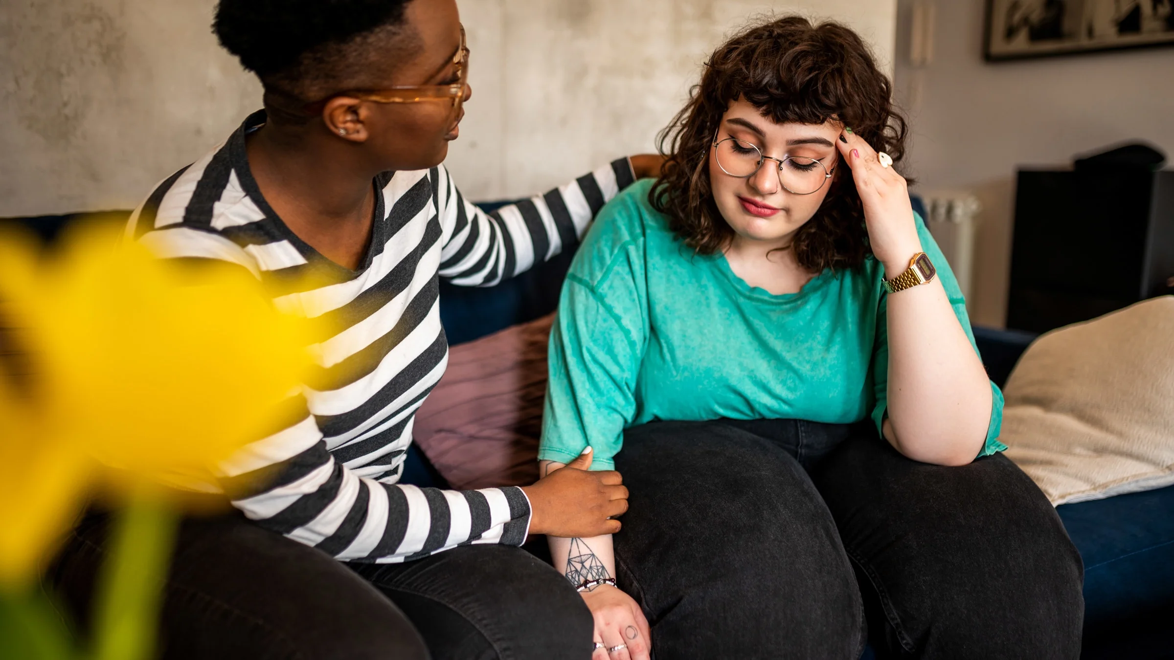 Two women sitting together on a couch. One is comforting the other.